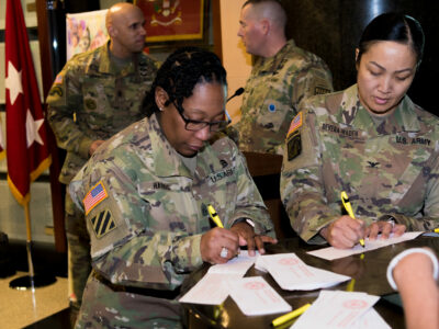 Two U.S. Soldiers in uniform stand at a table and fill out forms.