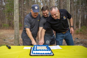 Three individuals cut a cake together.