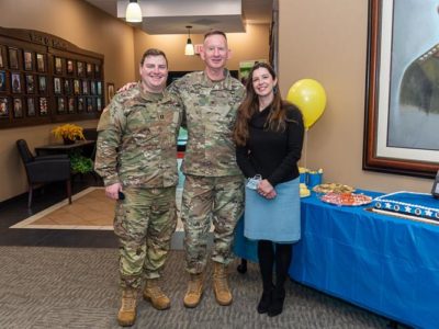 Two male soldiers and a civilian woman pose for a photo during an event.