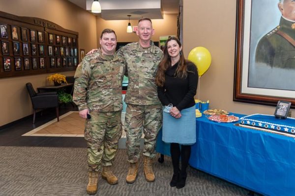 Two male soldiers and a civilian woman pose for a photo during an event.