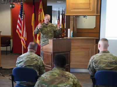 Army colonel stands at lectern and talks to a crowd of people.