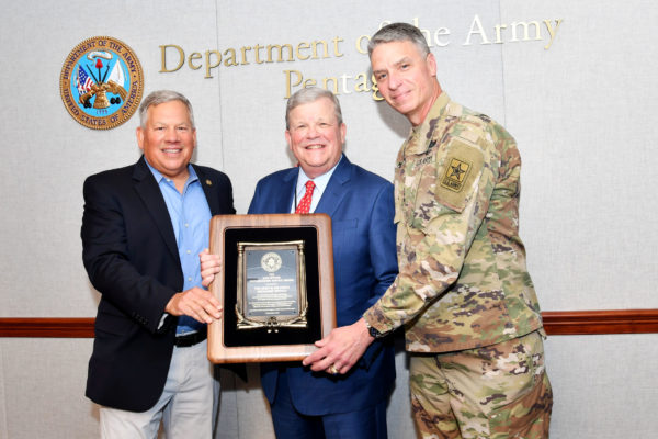 A man in a suit accepts an Army Emergency Relief award from another man in a suit and a U.S. Army general.