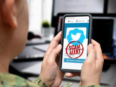 Close up photo graphic of a U.S. service member holding a smartphone with a scam alert on the screen.