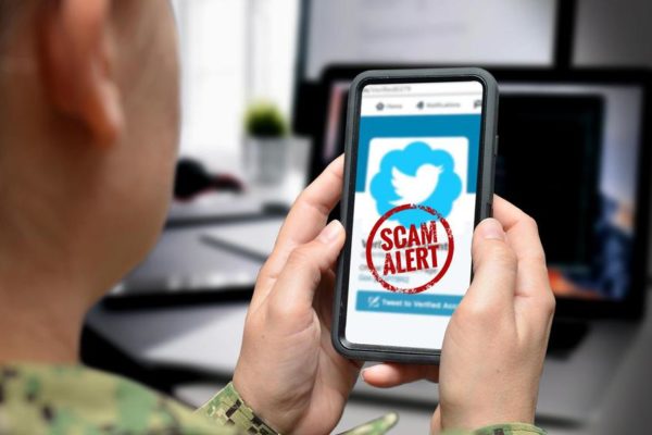 Close up photo graphic of a U.S. service member holding a smartphone with a scam alert on the screen.