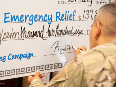 A man in a U.S. Army uniform signs a gigantic check.