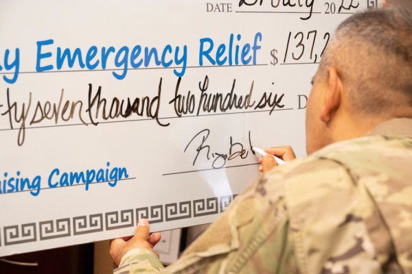 A man in a U.S. Army uniform signs a gigantic check.