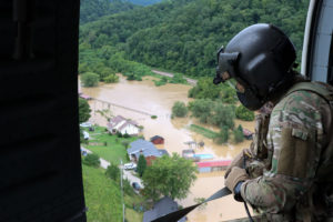 A member of the Kentucky National Guard looks out over flooded land in Kentucky from a helicopter.