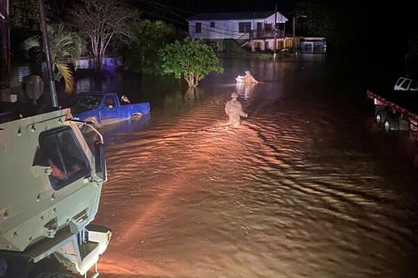 An Army truck sits in wheel-deep water as Soldier move toward a flooded house.