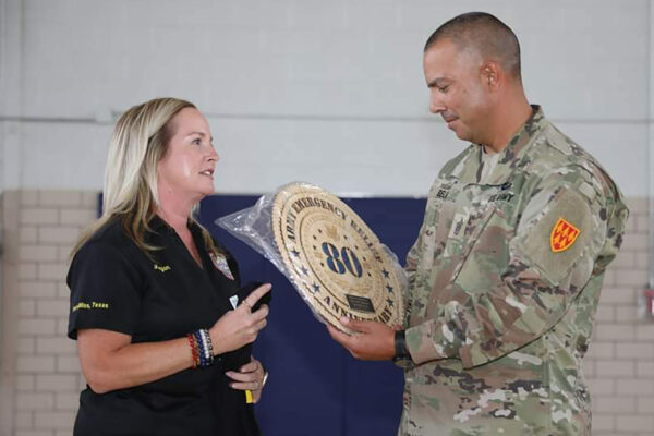 A woman hands a U.S. soldier in uniform a round wooden plaque.
