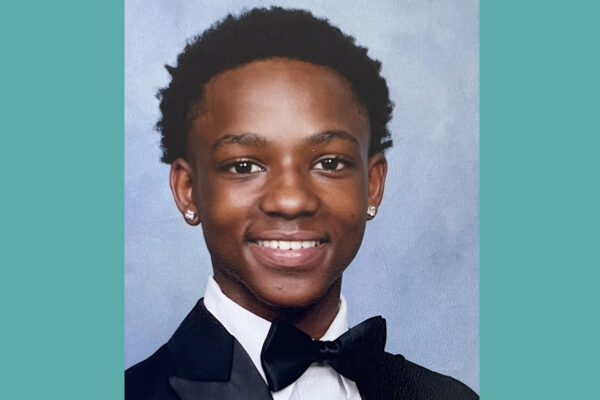 A boy wearing a black tuxedo and white dress shirt smiles for the camera.