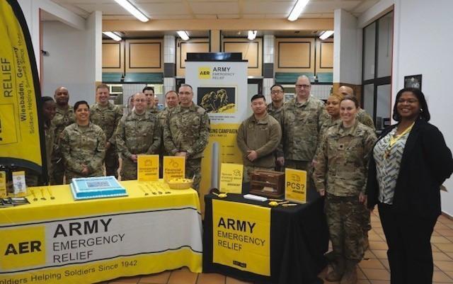Soldiers in uniform stand around a table displaying materials for Army Emergency Relief.