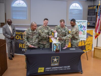 Four U.S. Soldiers in uniform put slips of paper into a donation box.