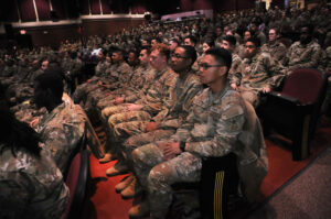 An audience of Soldiers in uniform sit in an auditorium.