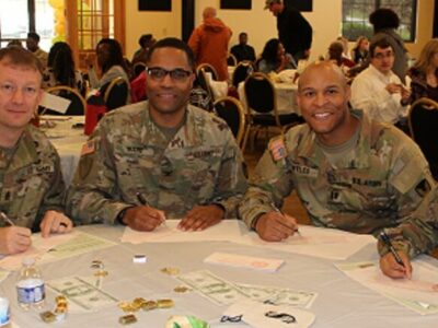 Four Soldiers in uniform sit at a table and look at the camera.