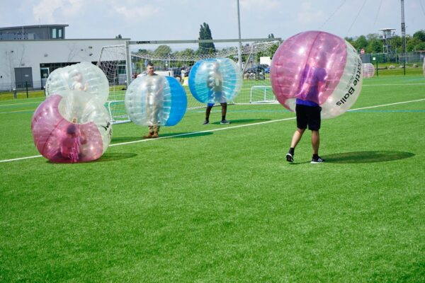 People run around a grassy field whilst inside of giant inflatable balls.
