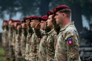 A line of Soldiers in uniform wearing red berets salute.