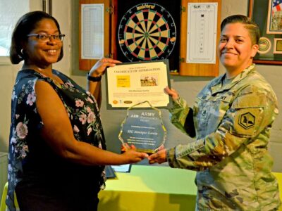 A civilian and U.S. Soldier in uniform hold a certificate and pose for a photo.